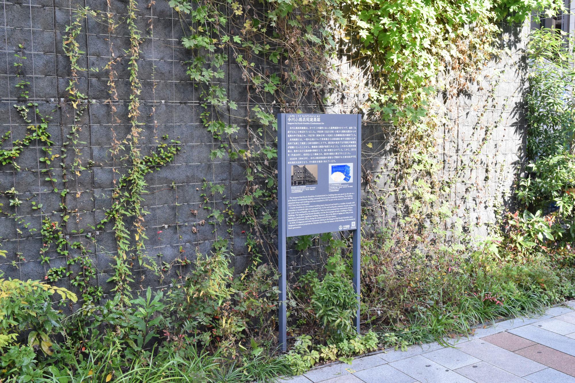 ツタが絡まる壁の前に設置された今川小路共同建築跡の説明板の写真