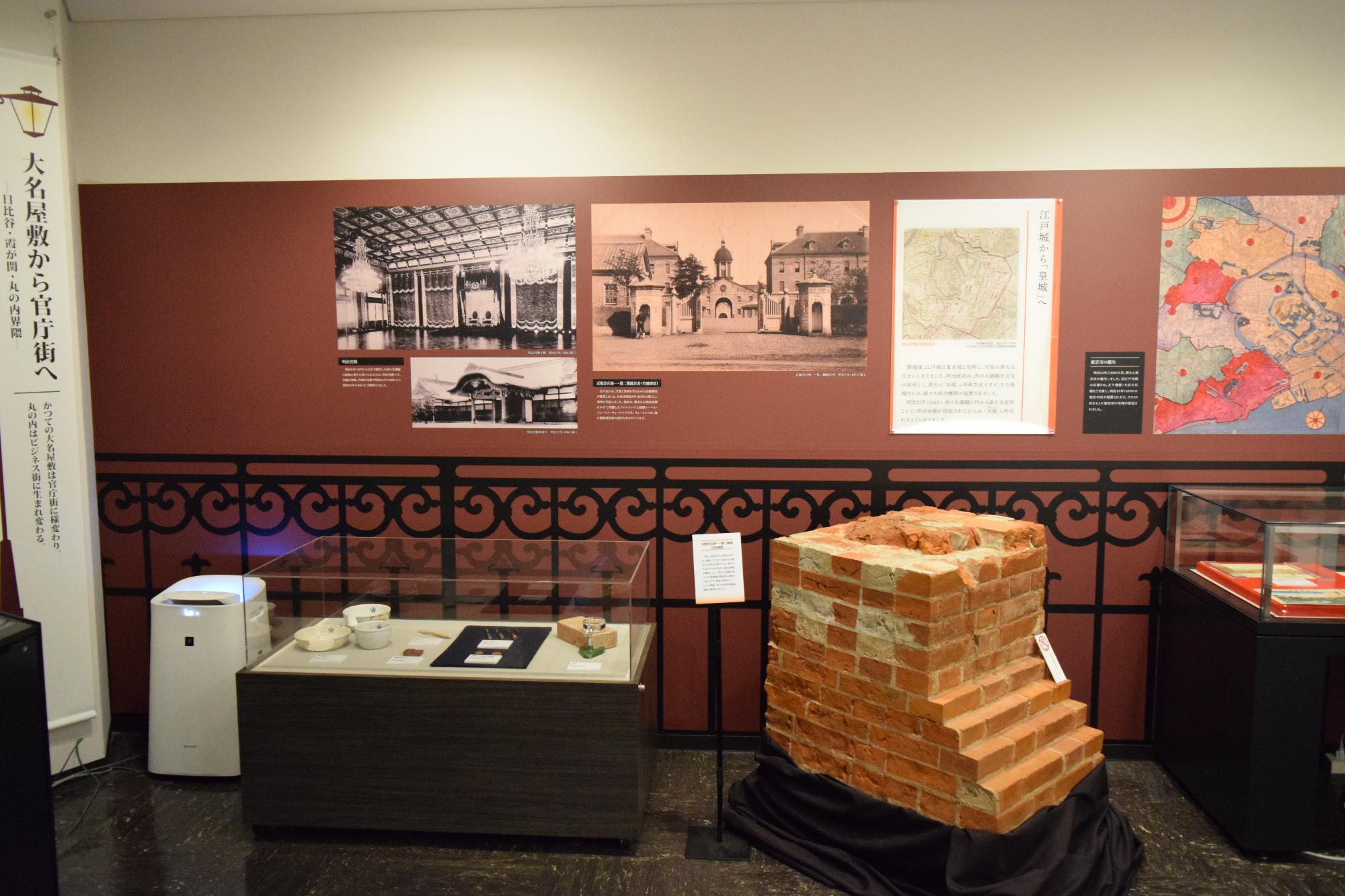 壁に建物の白黒写真や地図が貼られ、ガラスケースの中に展示された資料、出土した煉瓦が展示されている写真