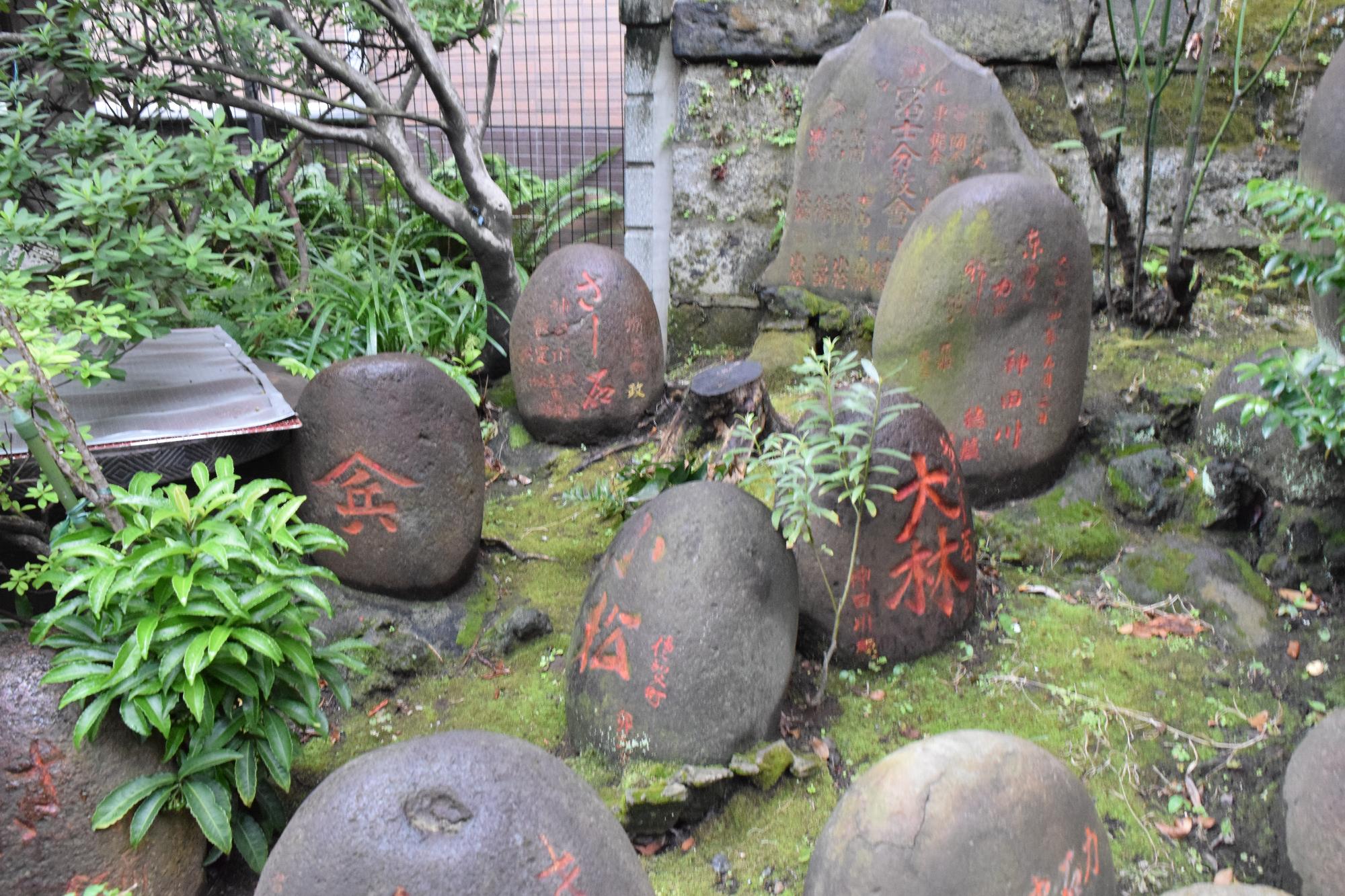 いろいろな形の石に赤で文字が刻まれている力石の写真
