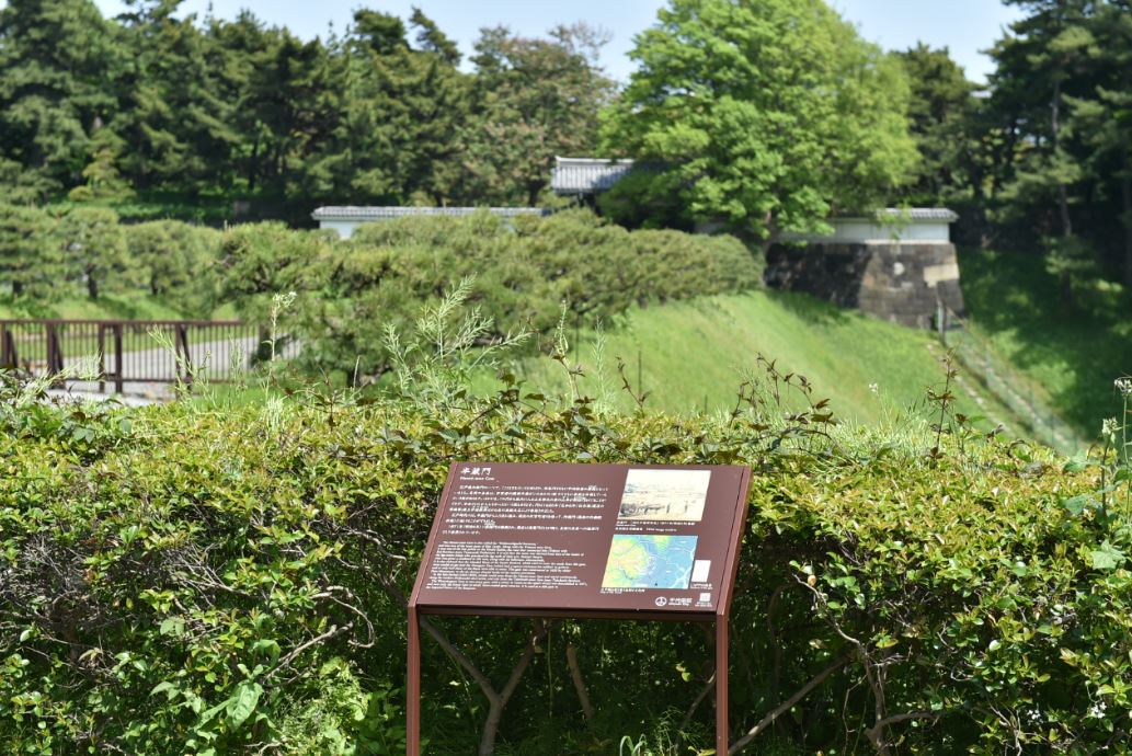 青々とした緑の木々や植木が立ち並び、半蔵門の説明板が設置されている写真