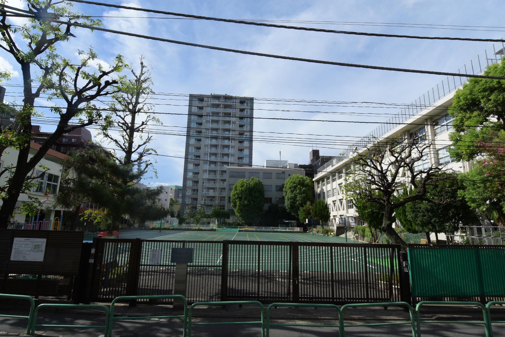 門扉が閉められ、正面に大きなコンクリート建物、右側に小学校の建物が建っている写真