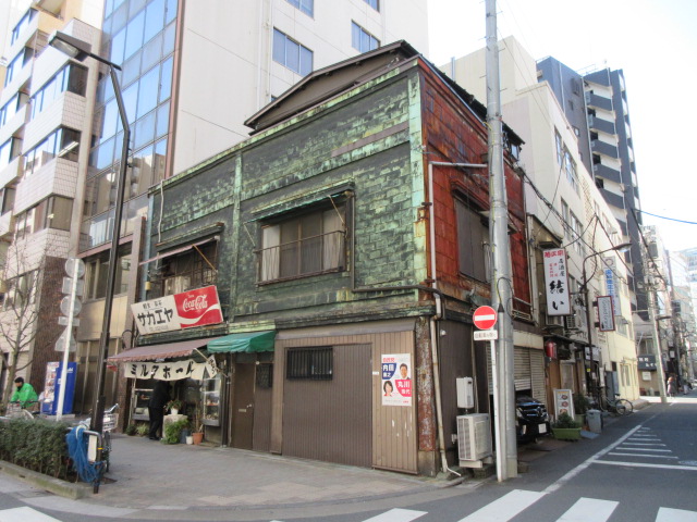 2階部分の立て板状の緑青が吹いた銅版のファサードが特徴的なサカエヤ店舗を道路反対側から写した写真