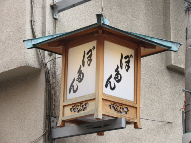 「ぼたん」と変体仮名で書かれた方形の軒行燈を正面から写した写真