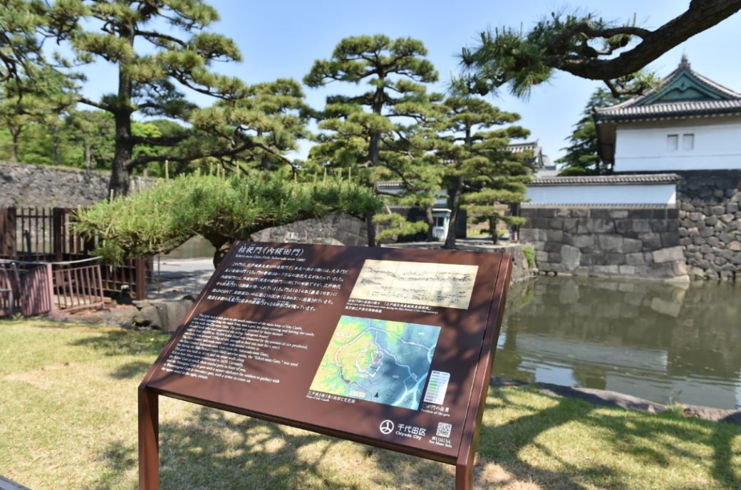 奥に内桜田門（桔梗門）の建物やが建ち、手前の土手に桔梗門（内桜田門）の説明板が設置されている写真