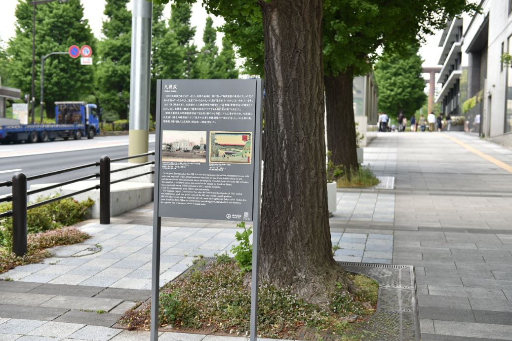 遊歩道の真ん中に木々が植えられ、九段坂の説明板が設置されている写真