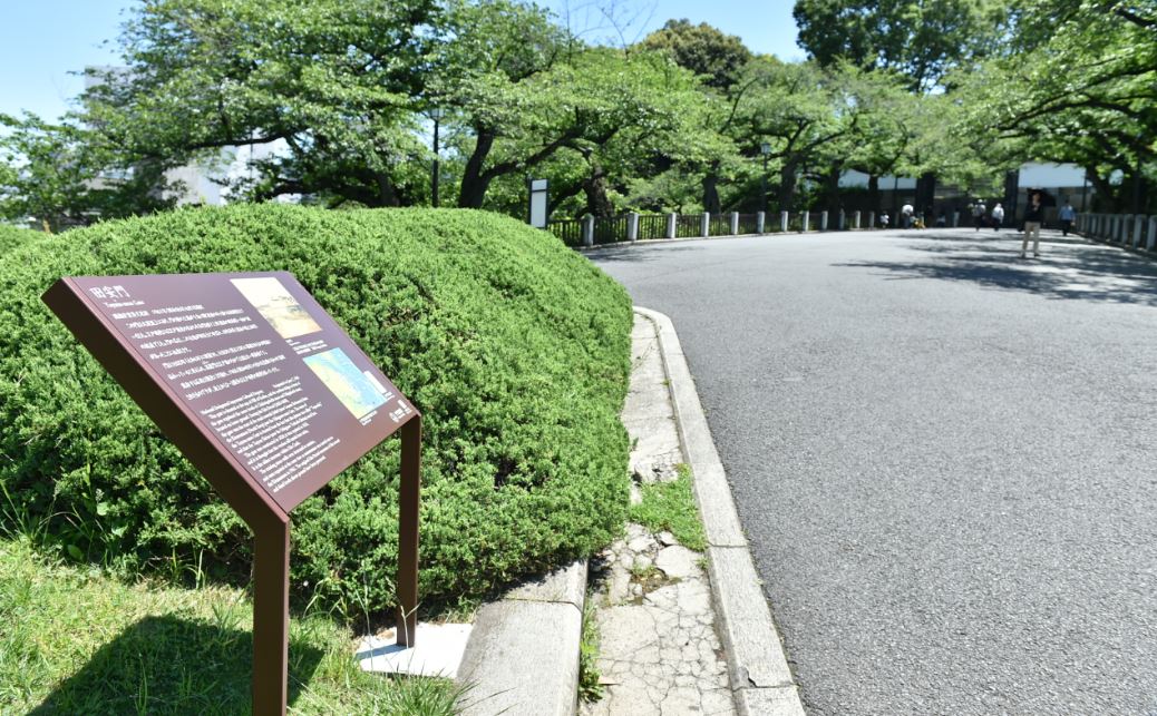 道路沿いのに植栽内設置された田安門の説明板の写真